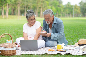 senior couple have a picnic and working with laptop computer in the park