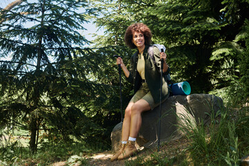 A young woman takes a break during her hike, sitting on a rock in the woods.