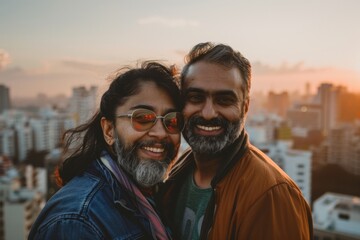 Portrait of a glad indian couple in their 40s wearing a trendy bomber jacket in front of vibrant city skyline