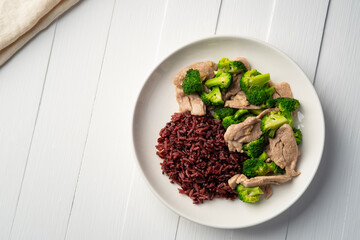 Cooked riceberry rice and Stir fried broccoli with pork tenderloin fillet in white plate.Thai Healthy food for low fat diet menu.Top view