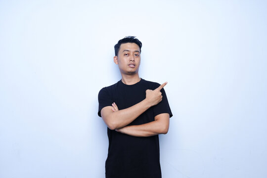 portrait of an Asian man pointing upwards. wearing a black t-shirt and a blue background.