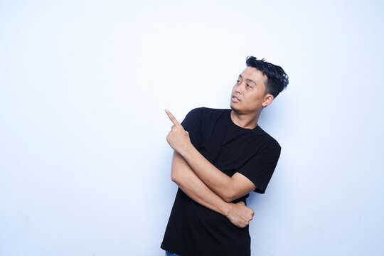 portrait of an Asian man pointing upwards. wearing a black t-shirt and a blue background.