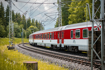 Modern electric passenger train enters the train station. Summer landscape in background. Red passenger wagons.
