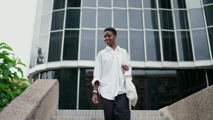 motivated young woman walks confidently through financial district, exuding joy and ambition. Dressed in white shirt with tote bag, female embodies modern success and positive outlook. Slow motion
