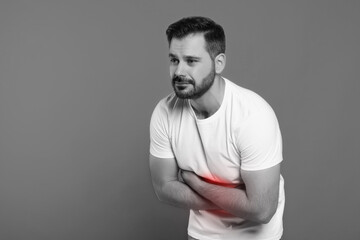 Man suffering from abdominal pain on grey background. Black and white effect with red accent