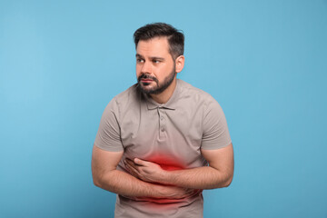 Man suffering from abdominal pain on light blue background