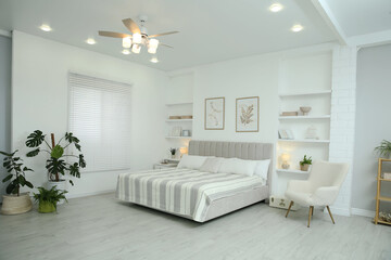 Comfortable furniture, ceiling fan, houseplants and accessories in stylish bedroom