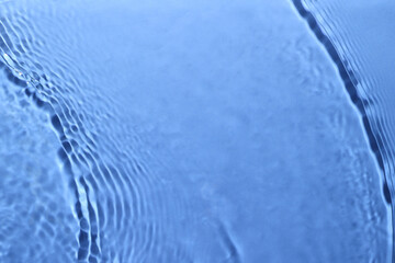 Rippled surface of clear water on light blue background, closeup