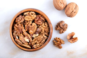 Walnut halves in a wooden bowl on a marble plate. Shelled and dried kernels, ripe seeds of the...