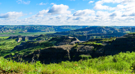 Fototapeta premium Lush greenery adorns the rugged terrain of a sprawling canyon under a vivid blue sky