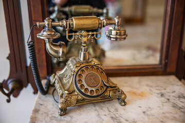 An old vintage antique gold dial up telephone for communication sitting on a marble dresser with a mirror