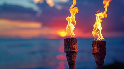 Two torches with flames against the sky at sunset. Two flaming tiki torches against a darkening sky with a soft sunset glow beginning, it must be the tropics.