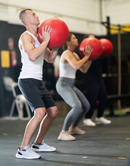 Sportive young man training with weight ball in sports hall during crossfit workout