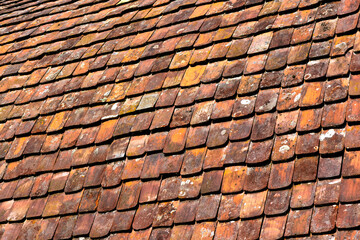 Colorful red and orange terracotta clay roof tiles of a historic monastery in Maulbronn, southern Germany. Aerial view with diagonal pattern of traditional tiles in bright sunlight. Grunge background.