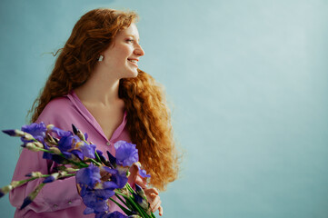 Beautiful happy smiling redhead freckled woman with long curly hair holding bouquet of iris...