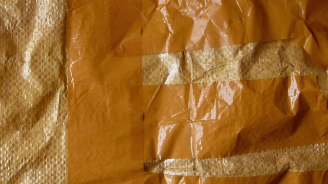 Orange plastic woven pp sack with stripes of adhesive tape motion video background. Dynamic changing used woven pp sack texture. Shipping bag grunge backdrop animation.