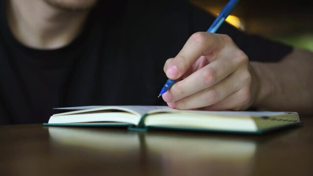 a man writes with a blue pen in a notepad.
Man with pen and notepad sitting at table