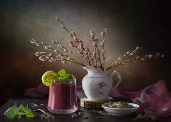 Still life with spring willow branches and kiwi smoothie in a glass on a wooden table