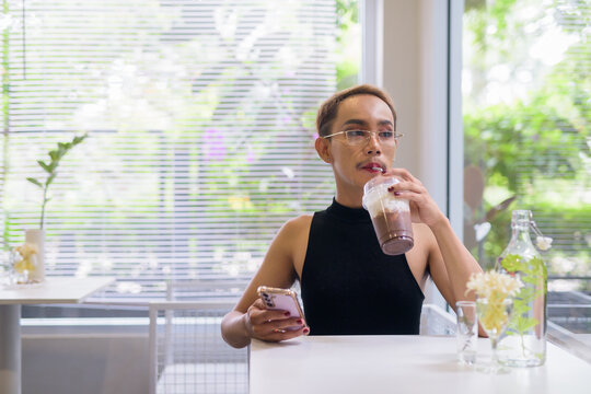 Beautiful Asian queer LGBT community supporter man using mobile phone in coffee shop