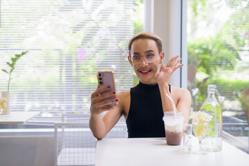 Beautiful Asian queer LGBT community supporter man using mobile phone in coffee shop