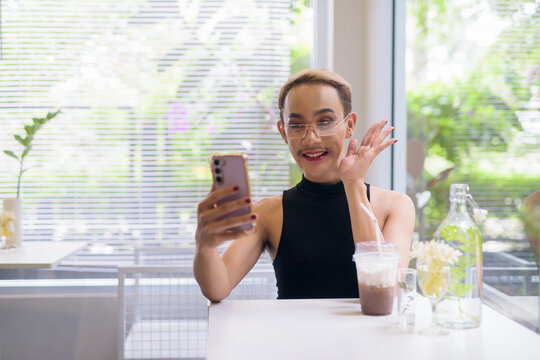 Beautiful Asian queer LGBT community supporter man using mobile phone in coffee shop