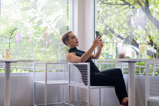 Beautiful Asian queer LGBT community supporter man sitting in coffee shop using phone