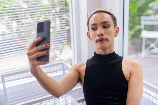 Beautiful Asian queer LGBT community supporter man taking selfie with mobile phone in coffee shop