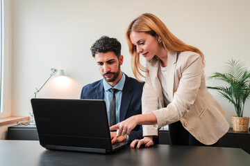 One business woman and a businessman working together with a laptop on a job project. Two real coworkers collaborating and planning using a computer. Teamwork of corporate employees on a brainstorming