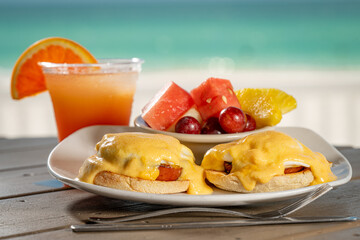 Eggs Benedict - two poached eggs on english muffin with ham topped with hollandaise and a side of fresh fruit.