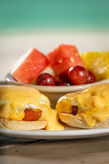 Eggs Benedict - two poached eggs on english muffin with ham topped with hollandaise and a side of fresh fruit.