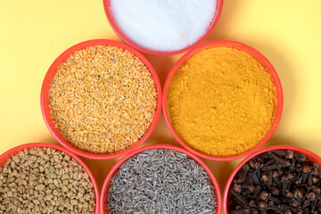 close-up view of red small bowls filled with salt, Fenugreek Seeds, turmeric powder, Mustard Seeds, Cumin Seeds, and Clove, Isolated on Black Background
