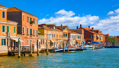 Obraz premium Murano Island in Venice, Italy. Antique italian houses on the channel with motorboats. Blue sky and white clouds murano. Sunny summer day. Popular touristic travel destination Europe