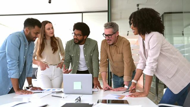 A diverse team of professionals is seen deeply engrossed in a laptop presentation, reflecting a moment of shared focus and collaborative analysis in a dynamic office setting