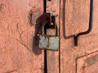 rusty metal padlock securing a latch on an old, weathered, and rusted metal door