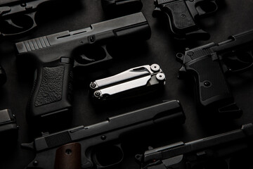 Silver multi-tool among various semi-automatic pistols. Dark back