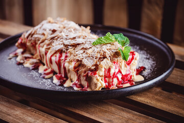 Puff pastry layered napoleon cake. Dessert with juicy vanilla cream and cherry raspberry filling, crumble served on a plate on table, wooden background. Restaurant dish. Specialty coffee aesthetics