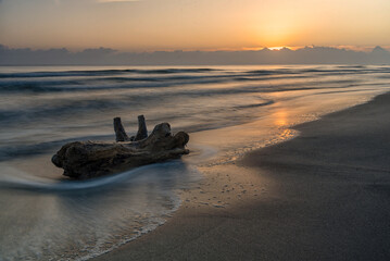 Alba sul mare con riflessi del sole sull'acqua e sulla sabbia e cielo nuvoloso.