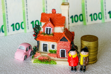 Scene with miniature toy figures, a young couple, residential house, a car, a pile of coins