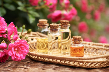 Bottles of aromatherapy essential oil with pink rose flowers outdoors