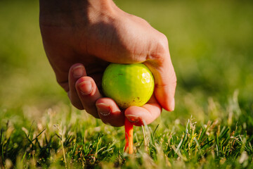 Valmiera, Latvia - June 3, 2024 - Close-up of a hand placing a yellow golf ball on a tee in the grass, ready for a shot, with a blurred background.