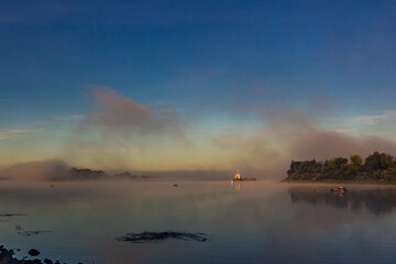 Fishermen on  boats early in the morning at dawn in the fog or mist at golden hour catch fish on...