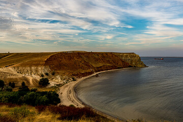 White Cirrus clouds in the blue sky on the Alexander graben. Steep cliff on the bank of the Volga River (Volgograd, Russia). Red clay, yellow sand on the beach, steep walls of the ravine.