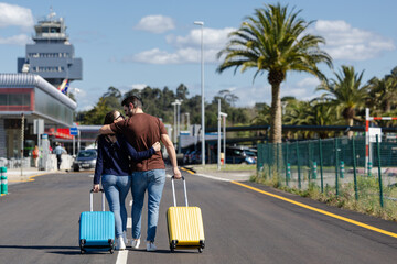 excited couple with their suitcases walking on the road on the way to the airport to go on summer vacation	
