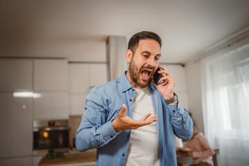 Exhausted angry man talk on mobile phone at home