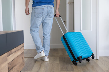 young man leaving home with his blue wheeled suitcase to go on a trip	