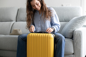 happy woman closing her suitcase sitting on the sofa at home to go on vacation