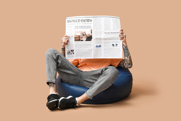 Man in beanbag chair with newspaper on beige background