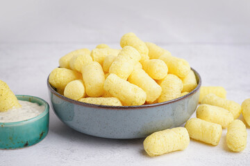 Bowl with tasty salty corn sticks and sauce on light background, closeup
