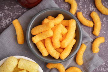 Bowls with different tasty salty corn sticks on grunge background, closeup