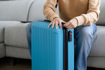 happy woman closing her suitcase sitting on the sofa at home to go on vacation